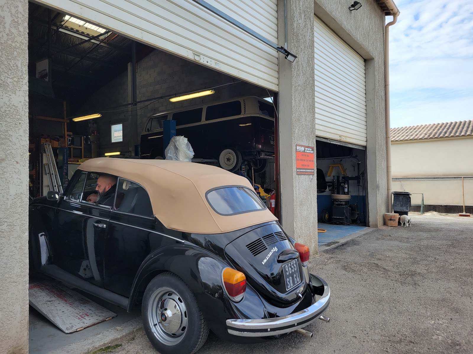 Une Citroën 2CV noire et beige en cours de restauration de carrosserie dans l'atelier.